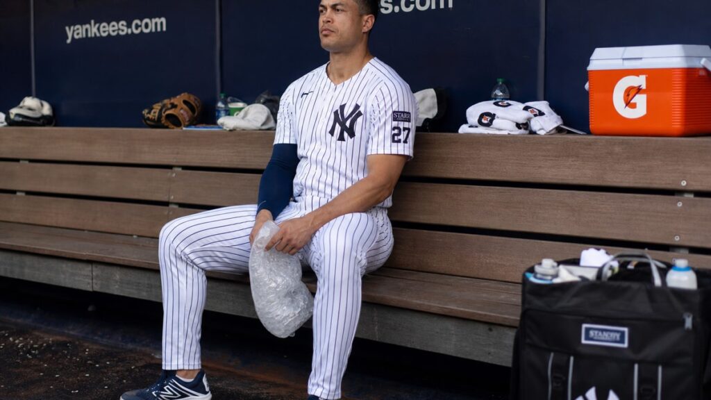 Giancarlo Stanton sitting in the Yankees dugout during his calf injury rehab