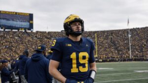 Michigan Wolverines quarterback in a number 19 jersey standing on the sideline at Michigan Stadium after Bryce Underwood was benched