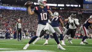 Drake Maye of the New England Patriots dropping back to pass under the lights in an NFL night game